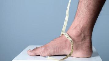 Close-up of a man measuring his foot size with a measuring tape against a light blue background photo