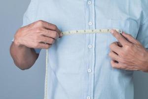 A man measures the width of his chest with a tape measure on a gray background. photo