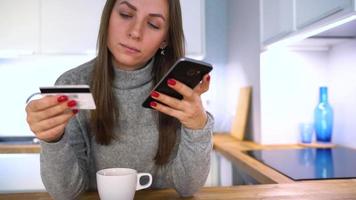 kvinna gör uppkopplad betalning på Hem med en kreditera kort och smartphone video
