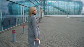Blonde girl rolls a suitcase near the airport terminal video