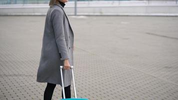blond flicka rullar en resväska nära de flygplats terminal video