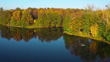 Aerial view of the lake, manor and the bright autumn forest on its shore. Forest is reflected on the surface of the lake video