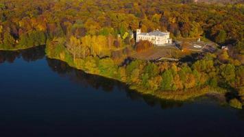 Aerial view of the lake, manor and the bright autumn forest on its shore. Forest is reflected on the surface of the lake video