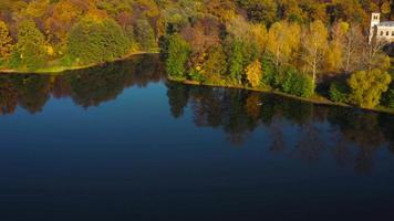 Aerial view of the lake, manor and the bright autumn forest on its shore. Forest is reflected on the surface of the lake video