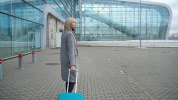 Blonde girl rolls a suitcase near the airport terminal video