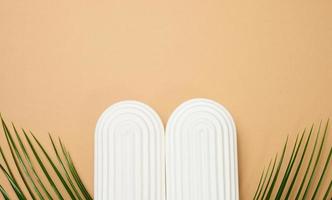 Green palm leaves and white decorative arches on a brown background, a stage for product display, cosmetics photo