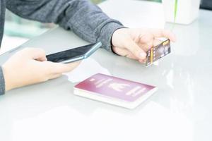 Woman sitting and using smartphone for online shopping with credit card and passport on deck in home office photo