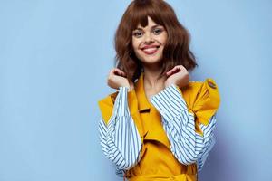 happy lady in a fashionable coat holds her hands bent near her face and smiles on a blue background cropped view photo