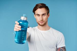 sporty man in white t-shirt holding blue water bottle in front of him studio photo