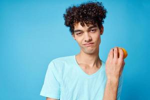 Cheerful guy with curly hair holding an orange fruit blue background photo