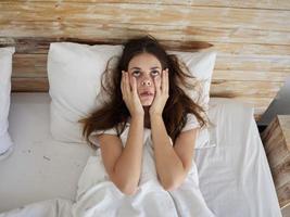 mujer acostado en cama debajo el cubre sostiene manos en cara emociones foto