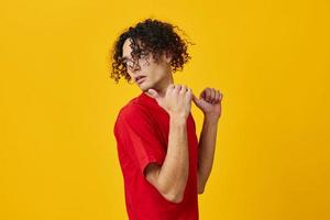 Confused funny Caucasian young man in red t-shirt point both hands aside posing isolated on over yellow studio background. The best offer with free place for advertising. Emotions for everyday concept photo