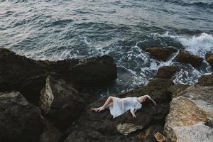 hermosa mujer en un blanco vestir acostado en un Roca en un blanco vestir ver desde encima foto