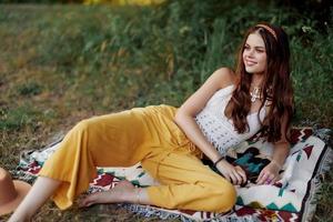 joven hermosa hippie mujer acostado en el suelo en naturaleza en el otoño en eco ropa en amarillo pantalones en el puesta de sol ligero foto