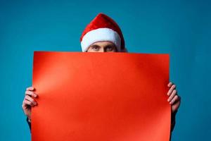 Cheerful man in a santa hat holding a banner holiday blue background photo