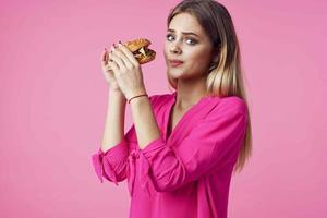 alegre rubia en un rosado camisa hamburguesa rápido comida bocadillo foto