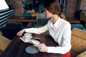 mujer en falda camisa a mesa en café café taza en mano y bloc bolígrafo foto