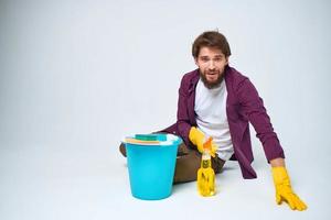 A man lies on the floor with a bucket of detergent cleaning service light background photo