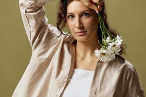 Happy pretty lovely curly beautiful female in linen casual shirt hold chamomiles flowers near cheek posing isolated on over olive green pastel background. Nature is beauty concept. Copy space photo