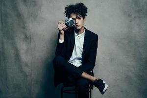 a man in a suit with a camera in his hands sits on a chair and chairs photo