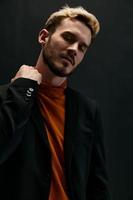 blond man in a coat and an orange sweater on a dark background photo