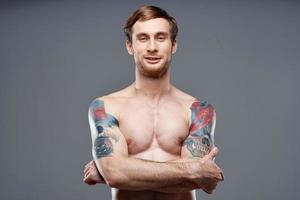 sexy carrocero con desnudo torso hecho de músculo tatuajes gris antecedentes cruzado brazos en cofre foto
