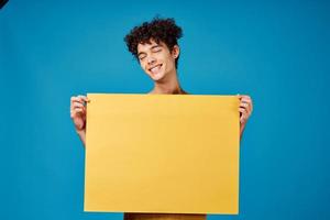 Cheerful man with yellow poster mockup blue background studio photo