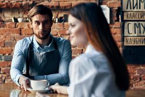 happy woman with a cup of coffee and male bartender in the apron at the table indoors photo