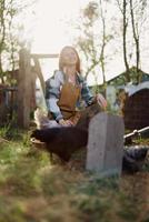 A woman sits in the bird pen and feeds the chickens organic healthy fresh food for the safety and health of the birds on the farm on a sunny summer day at sunset photo