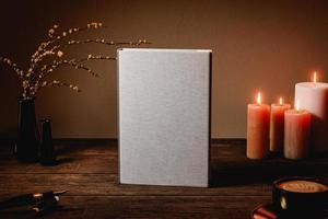 Hard cover book mock up on wooden table. Night interior with candles, plant and coffee. 3D rendering photo
