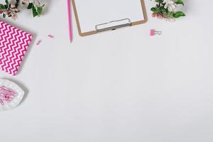 Home office desk workspace with blank paper clipboard, notepad, keyboard, stationery and apple tree flowers on white background with copy space photo