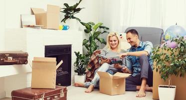 Beautiful young couple is higging, talking and smiling while sitting among cardboard boxes for moving photo