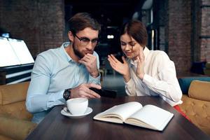 business man and woman sitting at a table in a cafe and looking at the phone photo