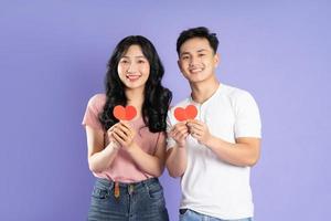image of asian couple holding a heart sticker, isolated on purple background photo