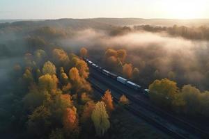 aéreo ver de carga tren en hermosa bosque en niebla a amanecer en otoño. vistoso paisaje con ferrocarril foto