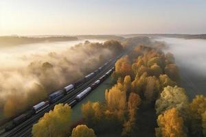 Aerial view of freight train in beautiful forest in fog at sunrise in autumn. Colorful landscape with railroad photo