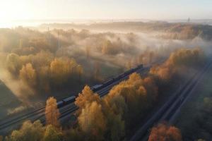 Aerial view of freight train in beautiful forest in fog at sunrise in autumn. Colorful landscape with railroad photo