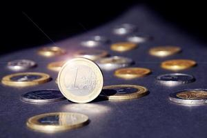 uno euro moneda en pie en borde brillante en destacar en contra muchos diferente monedas en oscuro antecedentes. dinero fluir foto