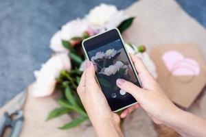 manos tomando móvil foto de flores, florista toma imagen con teléfono para social redes