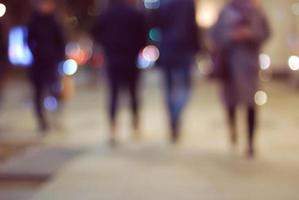 Blurry people silhouettes on night street in big city lights photo