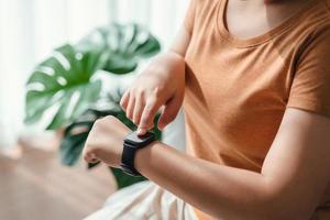 joven mujer mirando y utilizando un reloj inteligente, hembra sentado en el sofá comprobación su reloj inteligente. foto