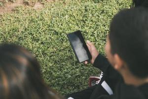 view from the back group of laughing Latinos sitting on the ground in a park with a smartphone photo