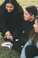 three people of Hispanic-Latino ethnicity, sitting on the ground in the park with smart devices photo