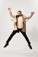 a successful man in a beige coat jumped up and gesticulates with his hands on a light background photo