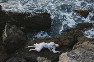 Barefoot woman in a secluded spot on a wild rocky coast in a white dress unaltered photo