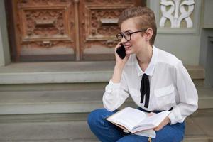 short haired woman with glasses walking around the city with a book education photo