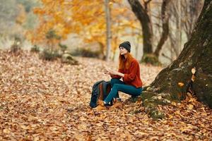 woman sitting near a tree in autumn forest and falling leaves landscape park photo