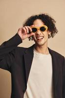 Defiant awesome tanned curly man in classic brown jacket trendy sunglasses posing isolated on over beige pastel background. Fashion New Collection offer. Retro style concept. Free place for ad photo