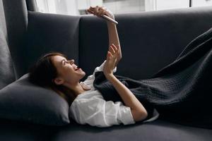 a pretty woman with a phone in her hands lies on a sofa in a room side view photo