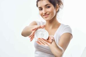 cheerful brunette in a white t-shirt with a jar of cream in her hands skin care light background photo